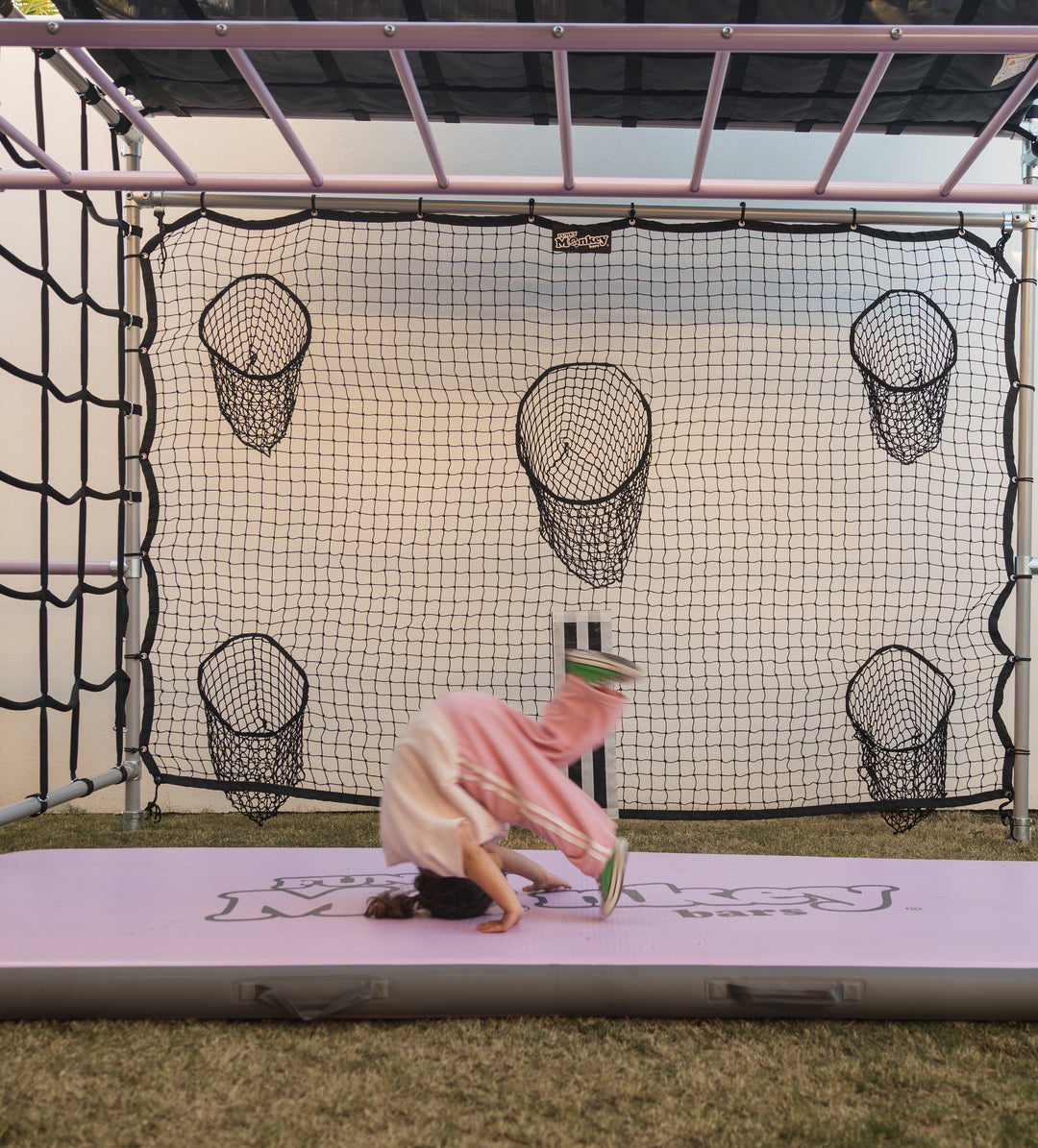 Child rolling on pink mat in front of soccer and cricket net on a Funky Monkey Bars frame
