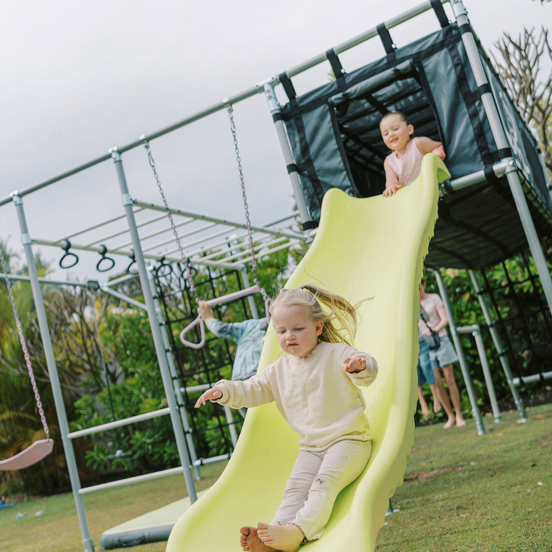 Children using yellow slide on Cubby Clubhouse attached to monkey bar frame