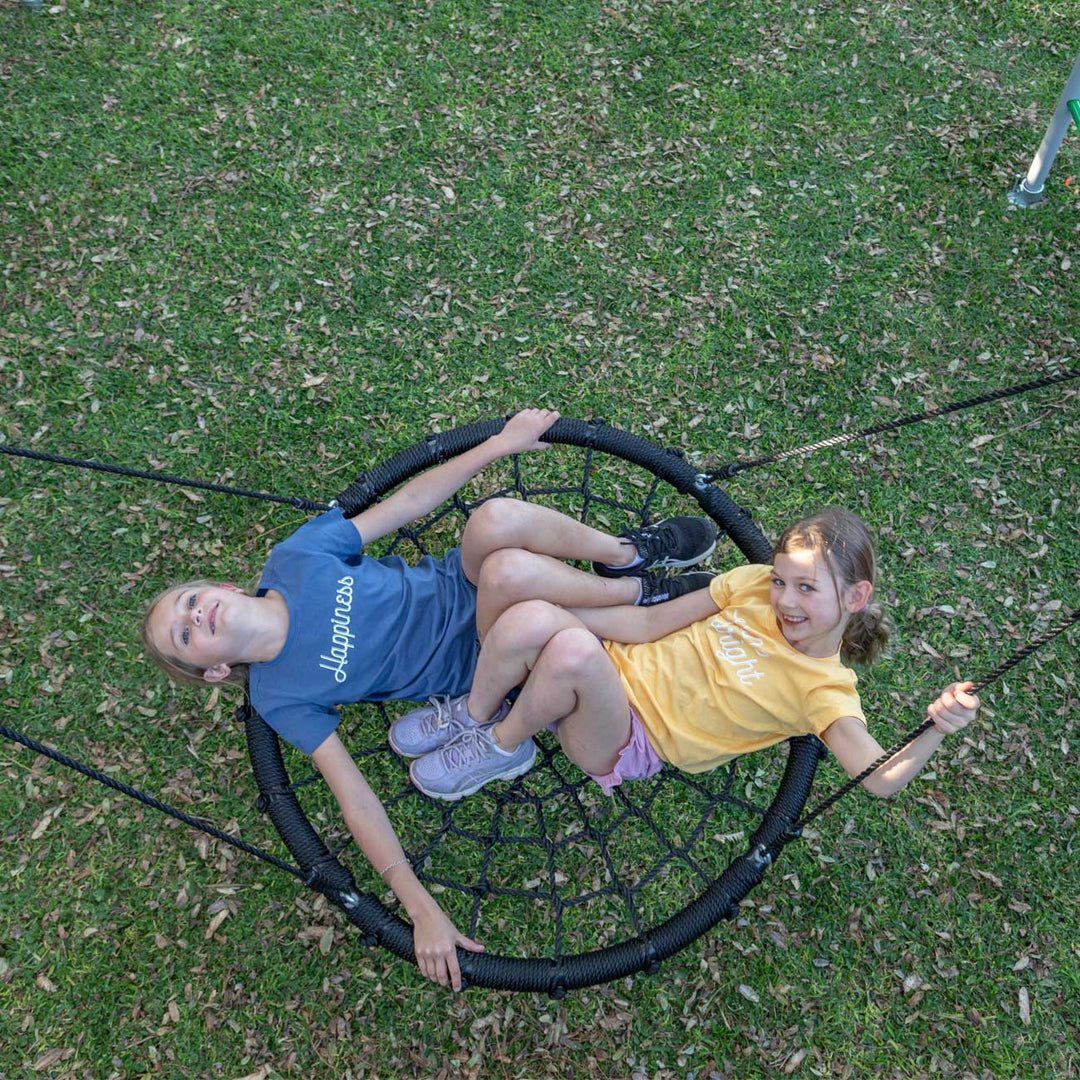 Two children lying in black Large Nest Swing on grass